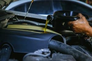 Car mechanic replacing and pouring fresh oil into engine at maintenance repair service station,