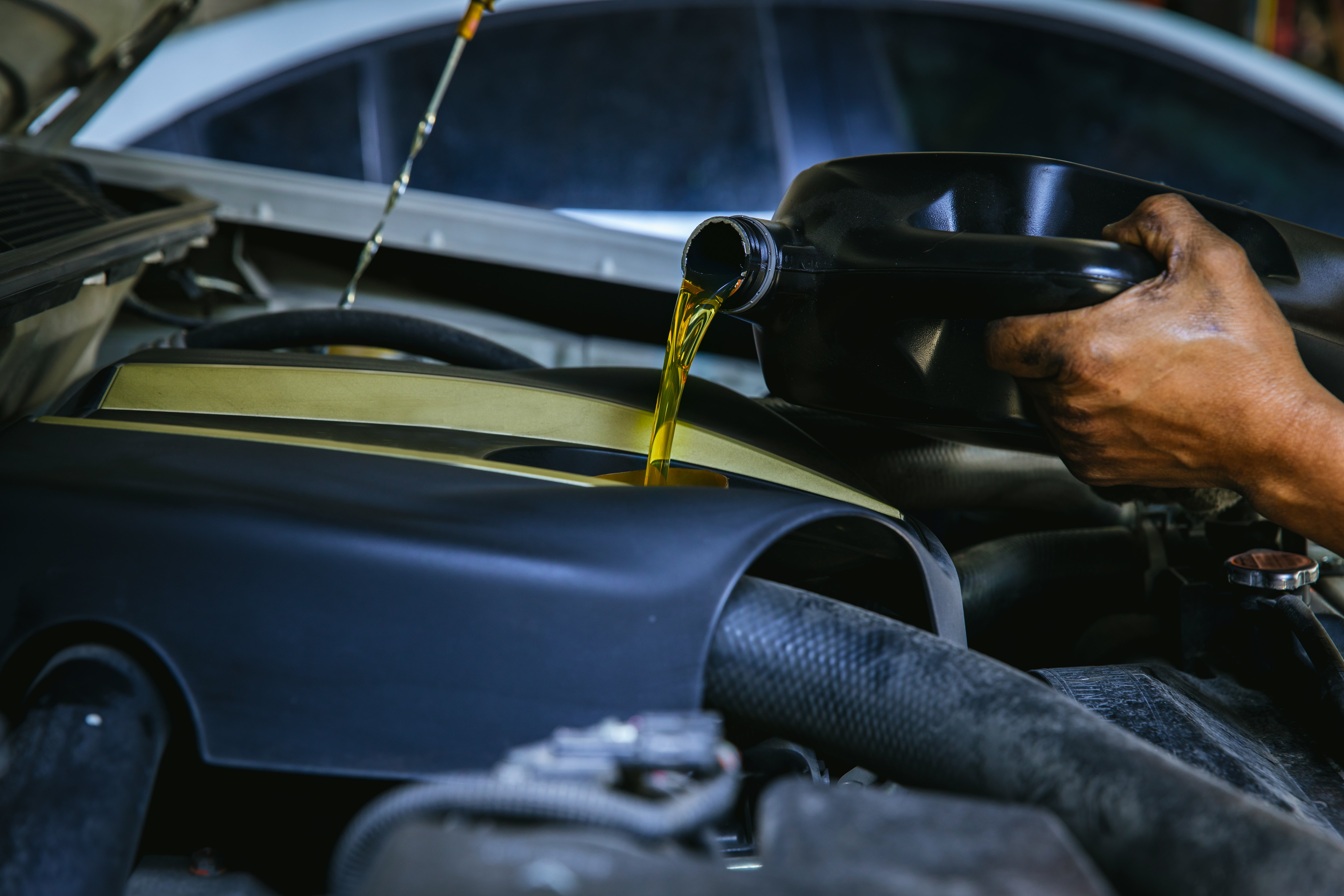 Car mechanic replacing and pouring fresh oil into engine at maintenance repair service station,